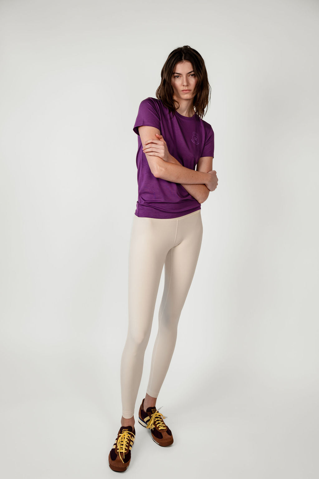 Woman wearing a purple shirt and beige leggings on a white background